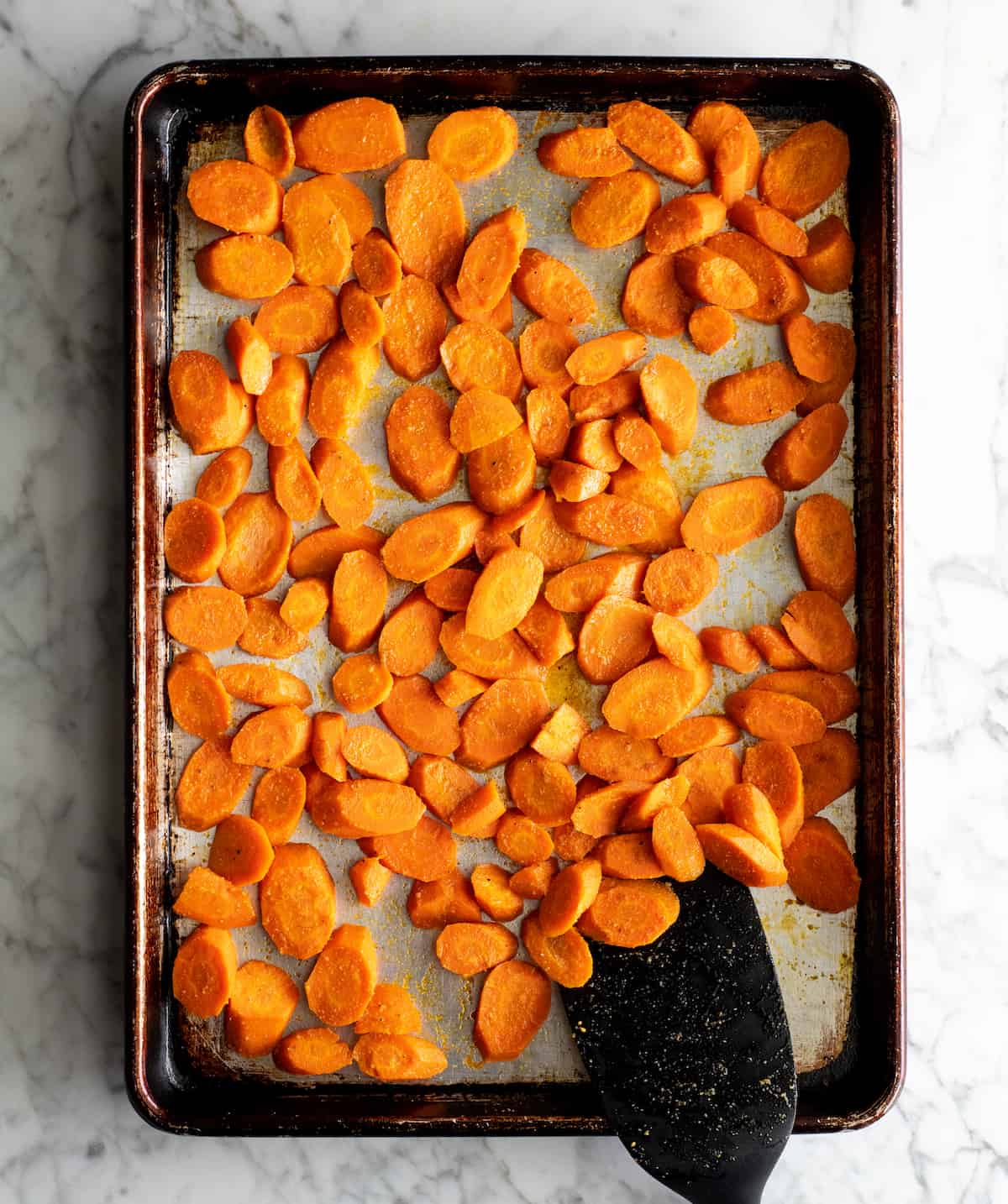 overhead photo showing how to roast carrots - spatula stirring roasted carrots on a baking pan