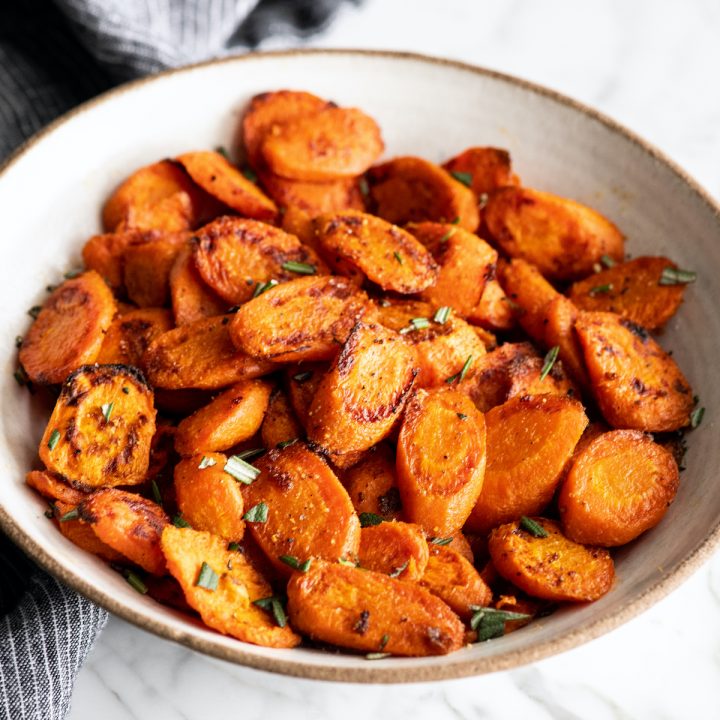 front view of roasted carrots in a bowl garnished with chopped rosemary