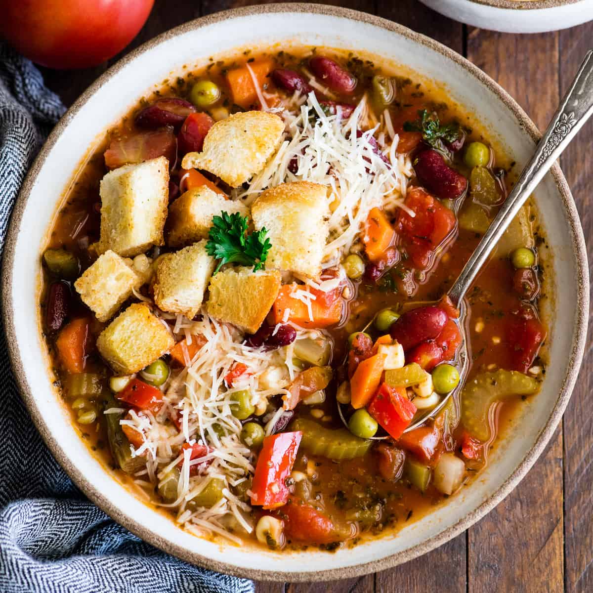 overhead view of a bowl of homemade vegetable soup topped with croutons and cheese with a spoon in it