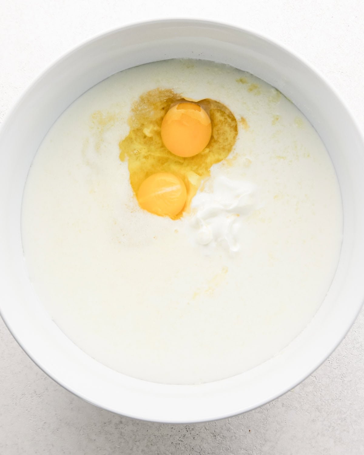 eggs, sour cream and milk added to the banana mixture in a white bowl to make banana cake