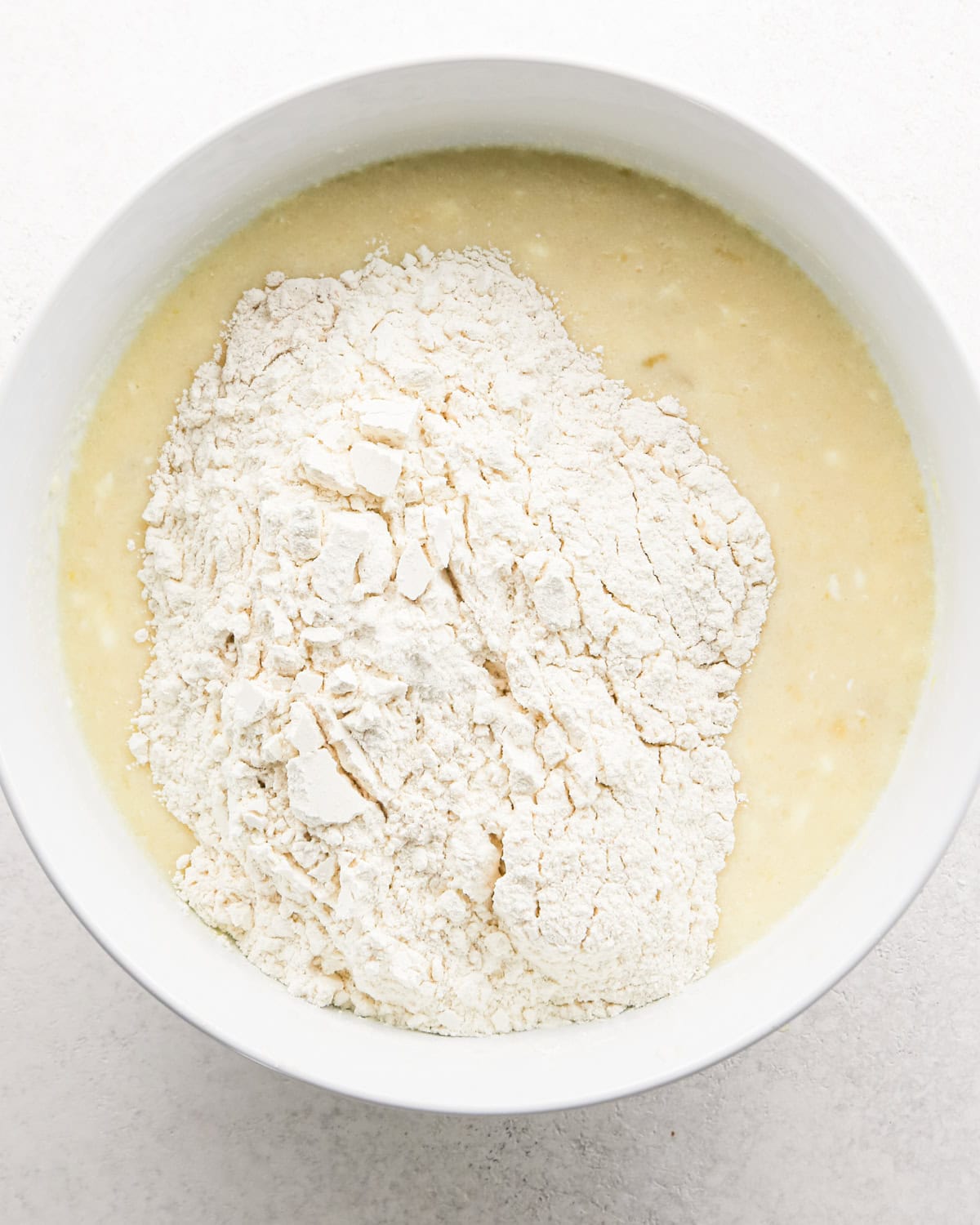 the dry ingredient flour mixture added to the wet ingredients in a white bowl before stirring to make banana cake