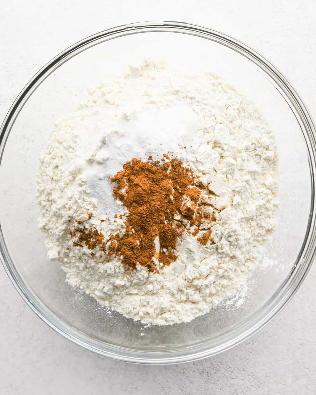 A glass bowl with flour, baking soda, and ground cinnamon, showing the dry ingredients before mixing for banana cake batter.