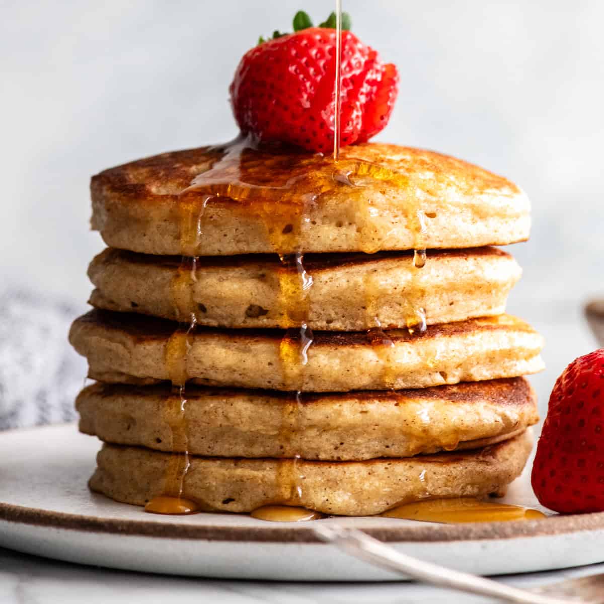 front view of a stack of 5 whole wheat pancakes with syrup pouring onto them