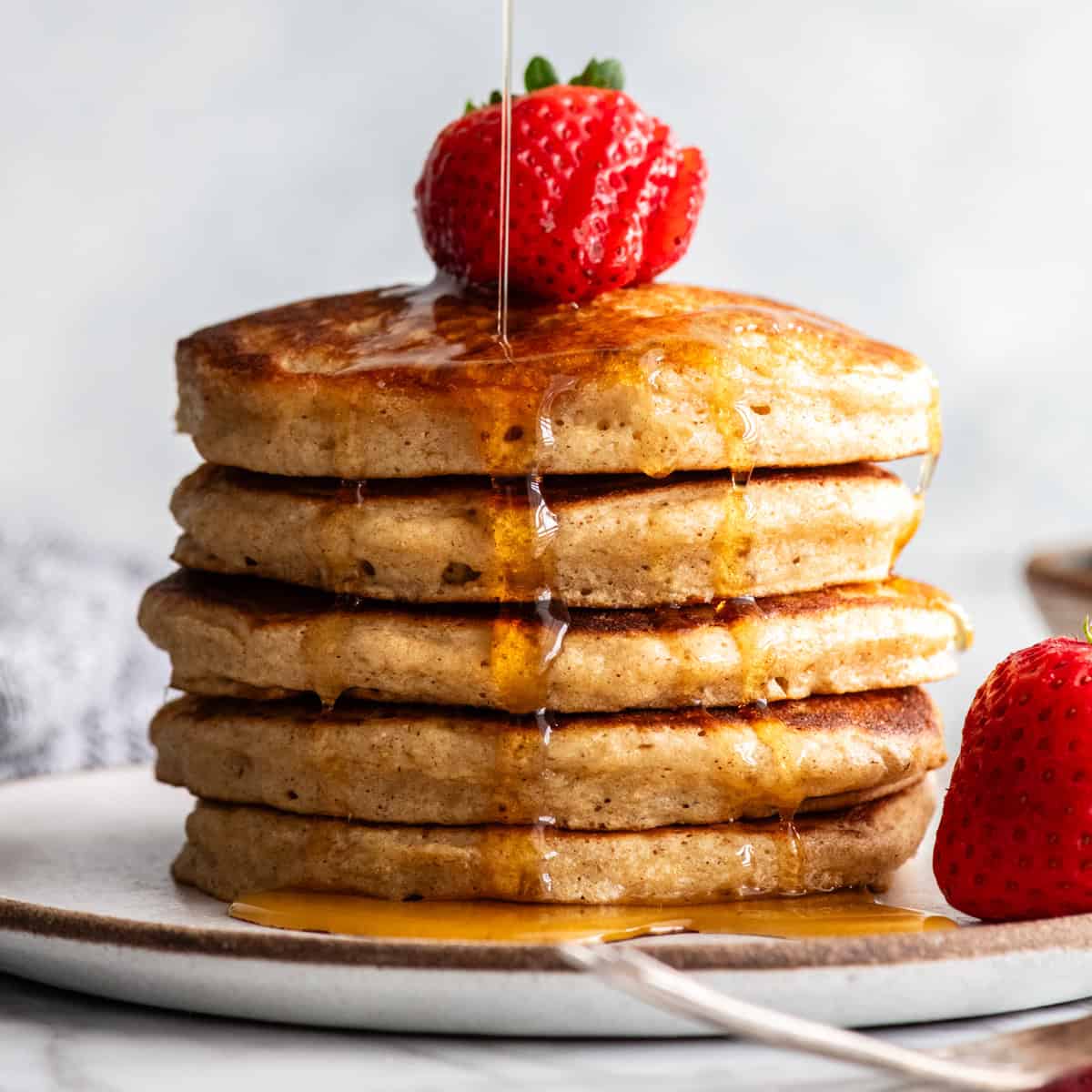front view of a stack of 5 whole wheat pancakes with syrup pouring on them