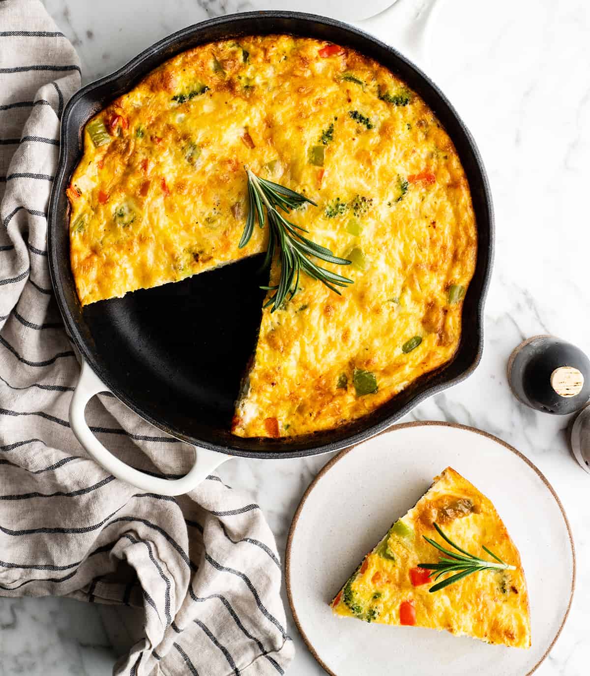 overhead photo of a frittata in a skillet with a piece of it cut out on a plate next to the skillet
