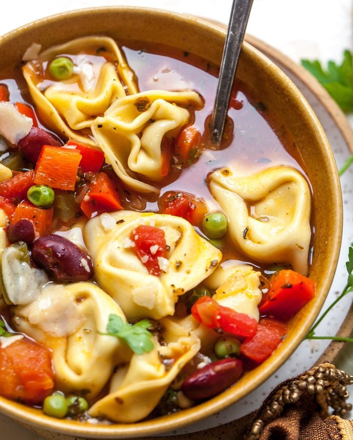 a bowl of tortellini soup with a spoon in it
