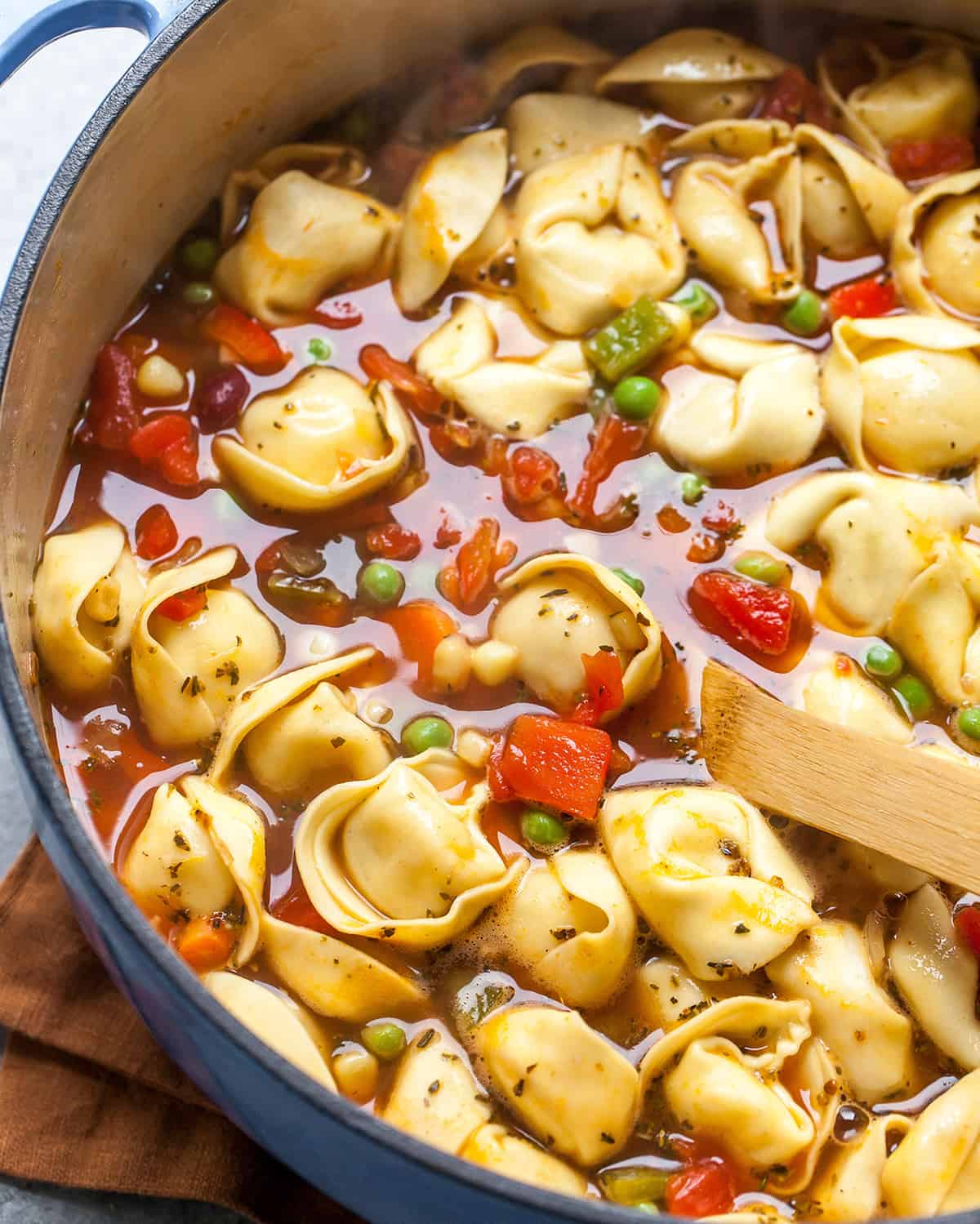 tortellini soup in a pot with a wooden spoon