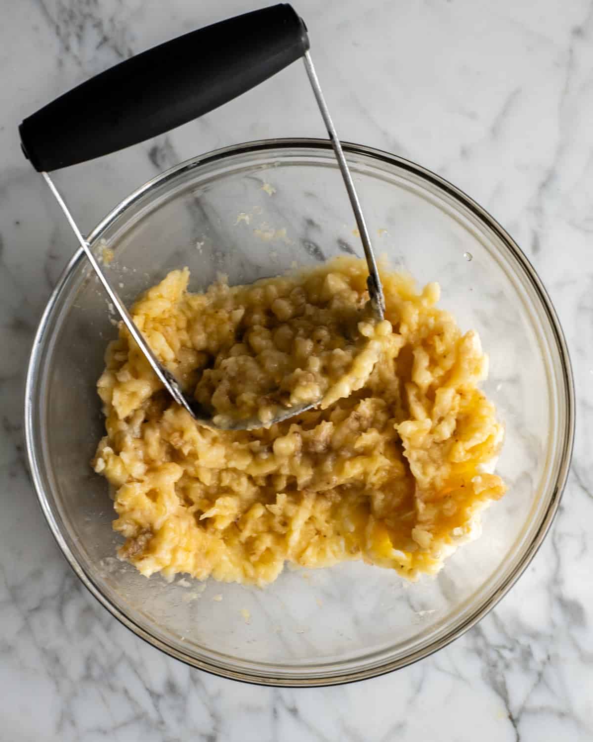 mashed banana in a glass bowl with a potato masher