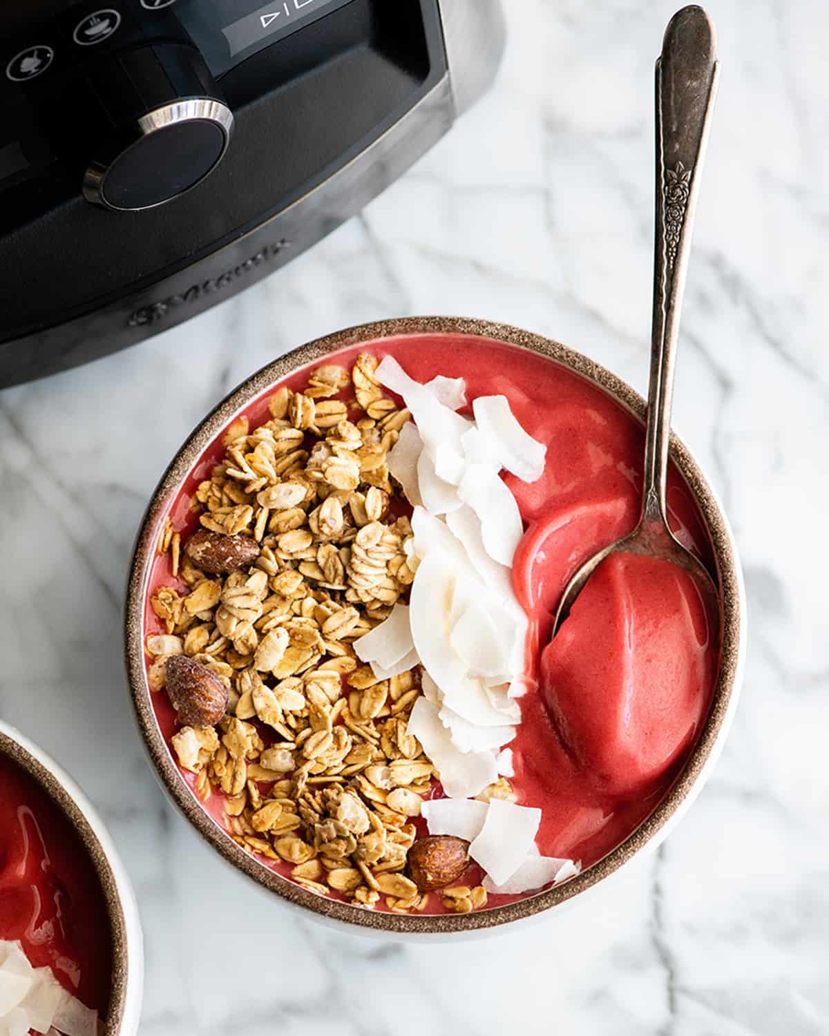 overhead photo of a smoothie bowl with a spoon, granola and coconut 