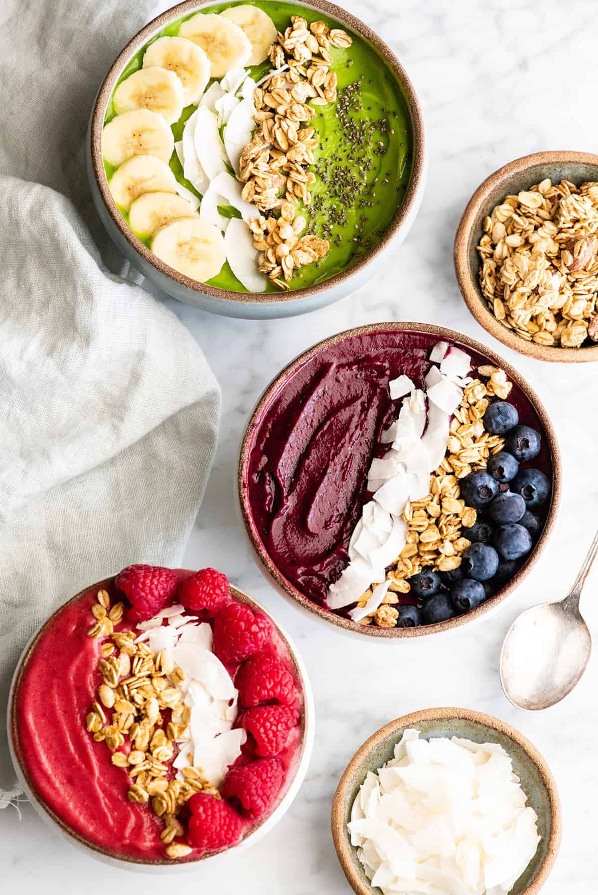 overhead view of three smoothie bowls with toppings - one green one purple and one pink 