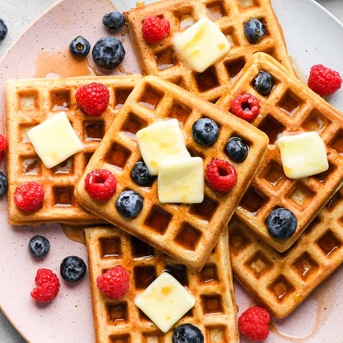 6 waffles on a plate with syrup, butter and berries