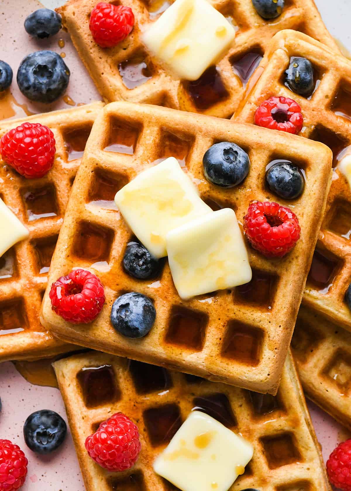 6 waffles on a plate with syrup, butter and berries