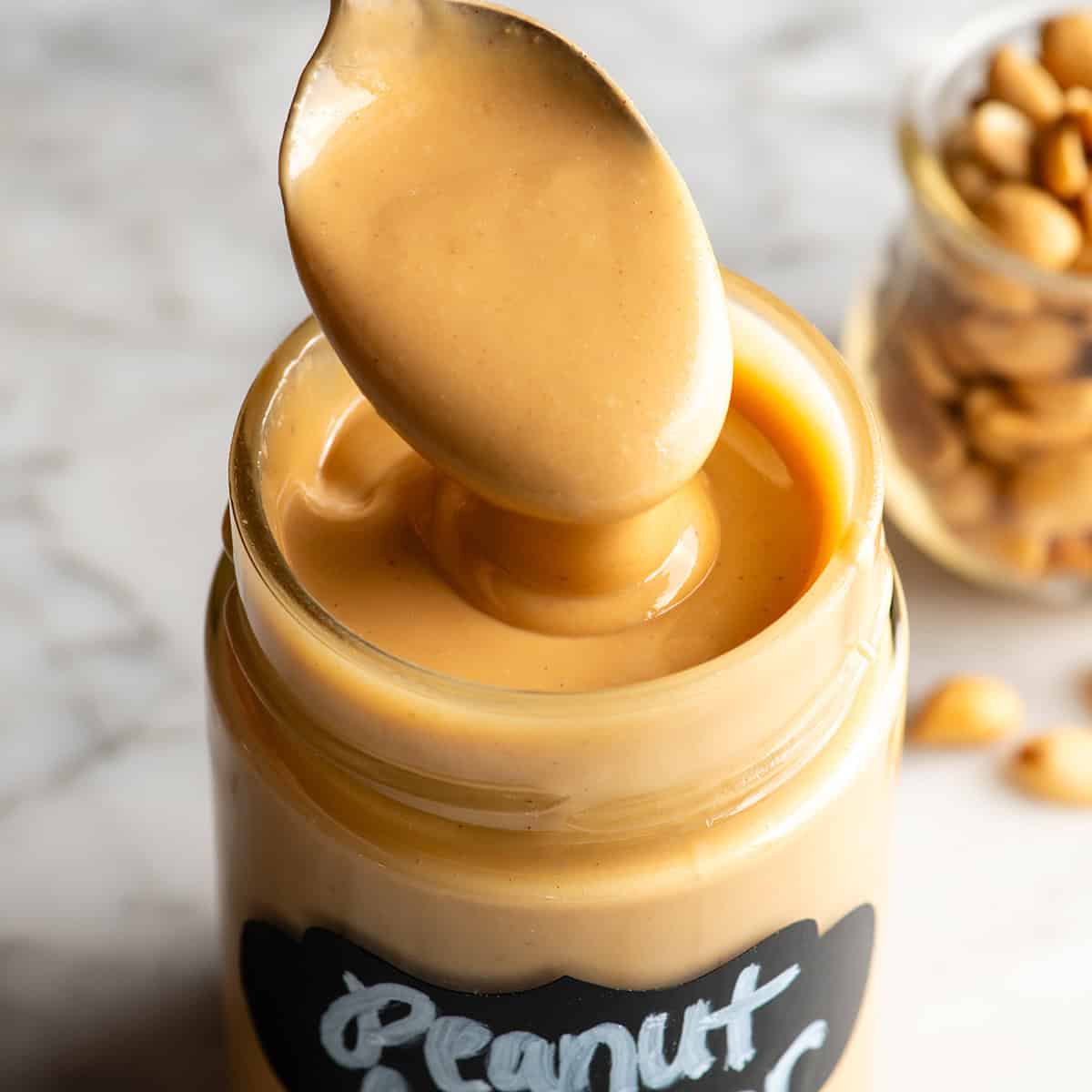 a spoon taking a scoop of homemade peanut butter out of a labeled glass jar