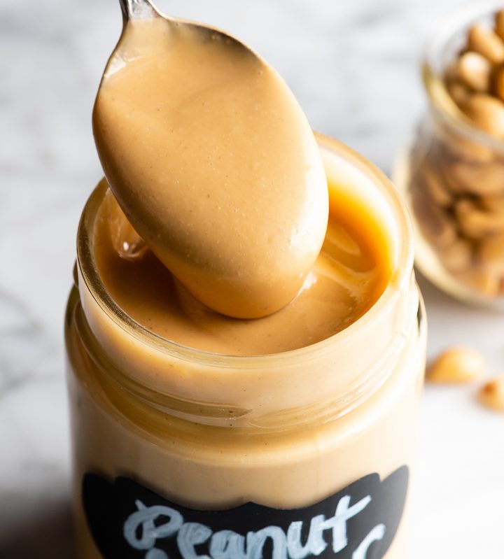 a spoon taking a scoop homemade peanut butter out of a glass jar