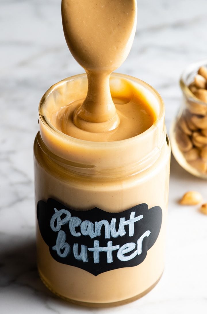 a spoon drizzling homemade peanut butter into a jar