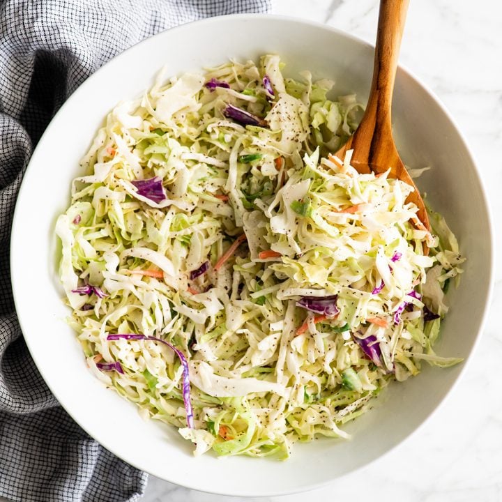 a spoon scooping homemade coleslaw out of a large bowl
