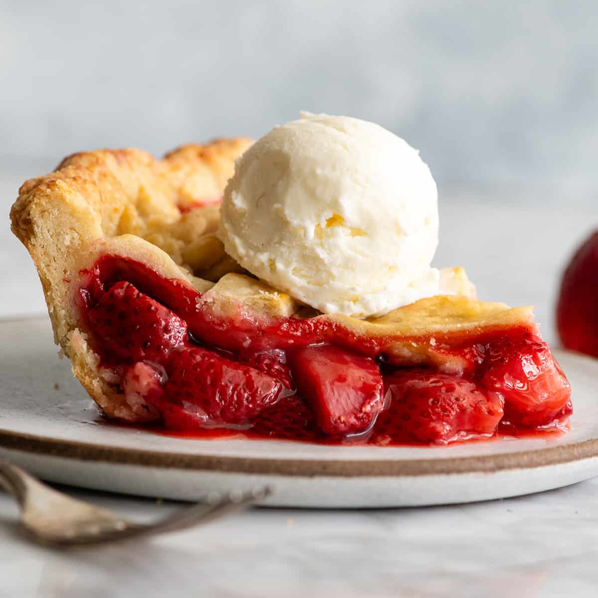 side view of a slice of strawberry pie with a scoop of ice cream on top