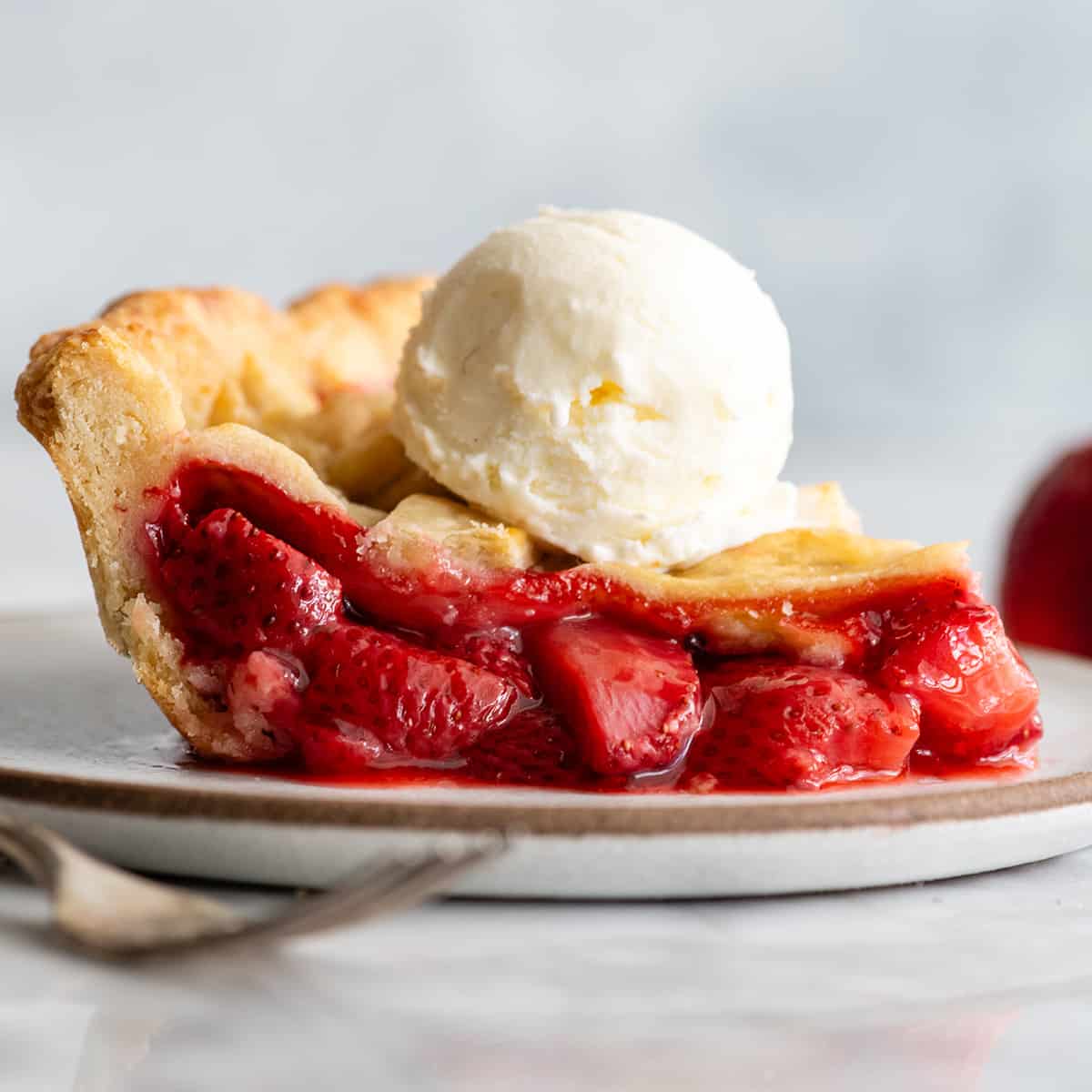 side view of a slice of strawberry pie on a plate with vanilla ice cream on top
