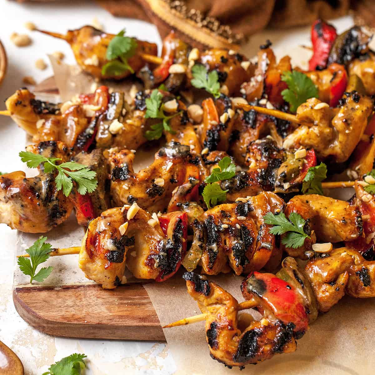 grilled chicken satay skewers on a serving board garnished with peanuts and cilantro
