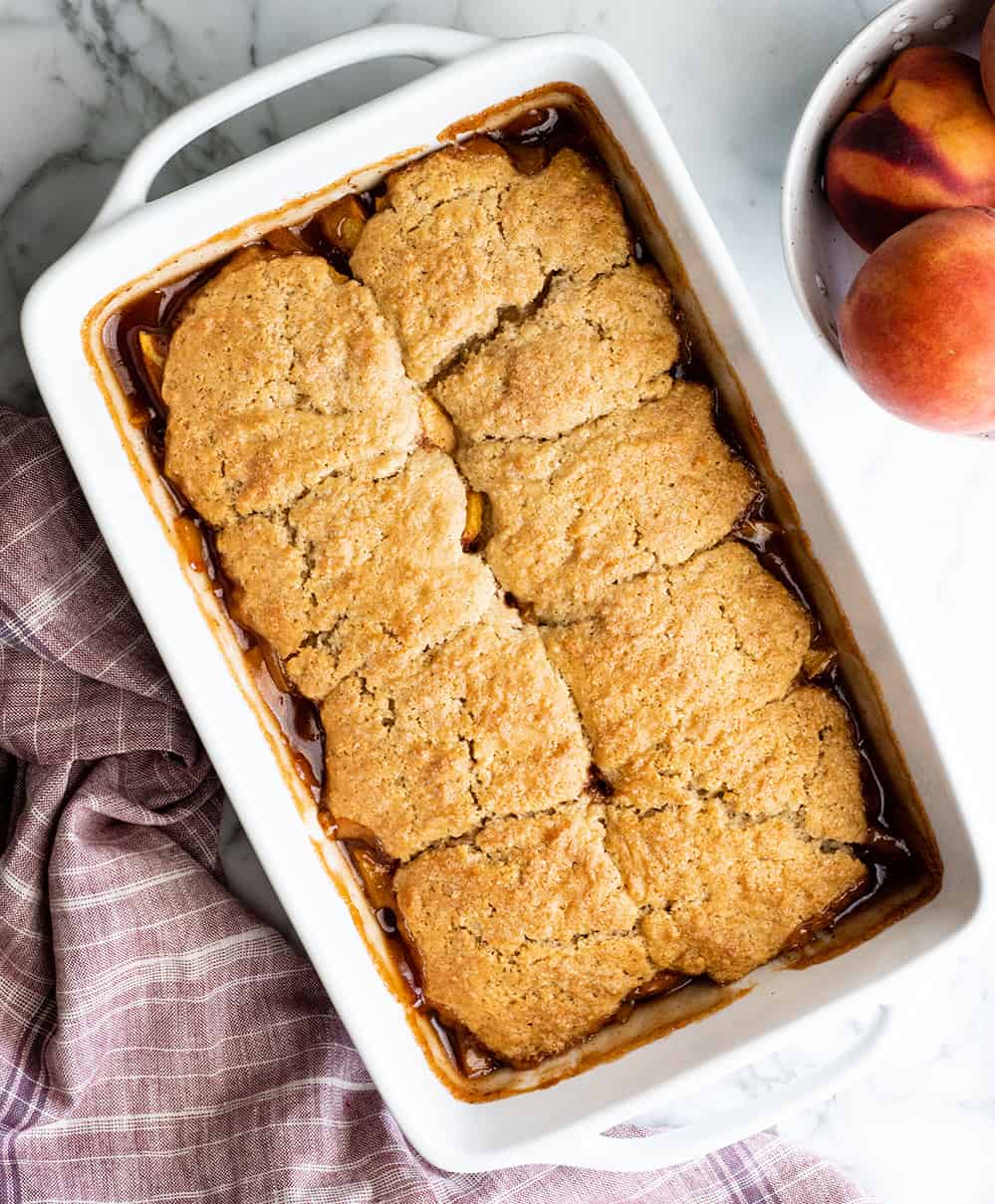 overhead view of a baked peach cobbler in a white baking dish