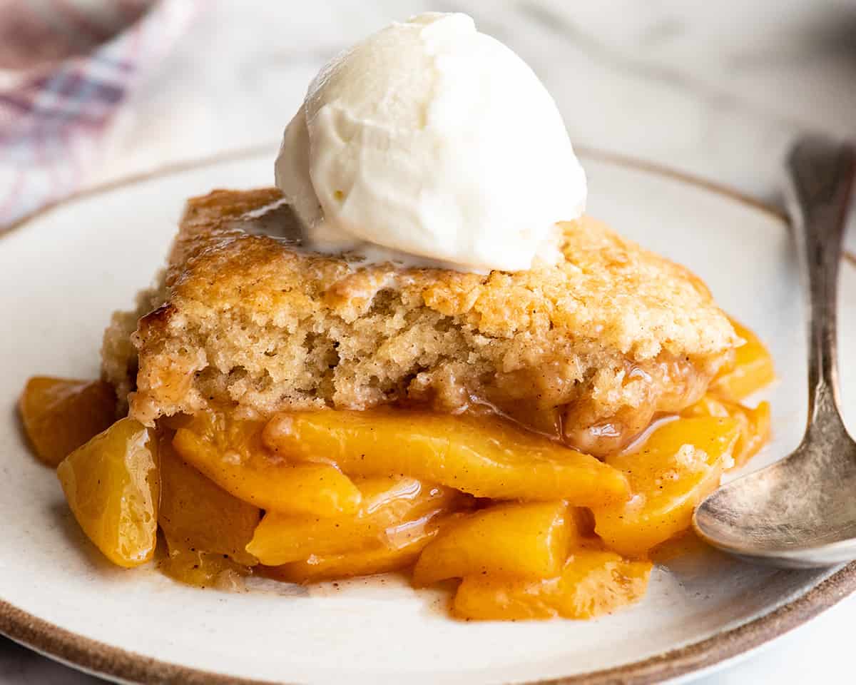 front view of a piece of peach cobbler on a plate with vanilla ice cream on top