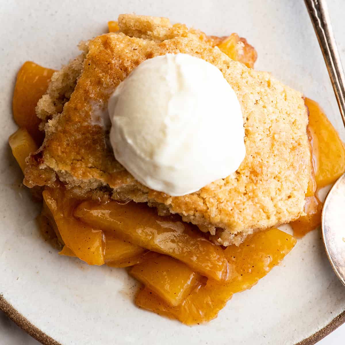 overhead view of a piece of peach cobbler with vanilla ice cream on top on a plate