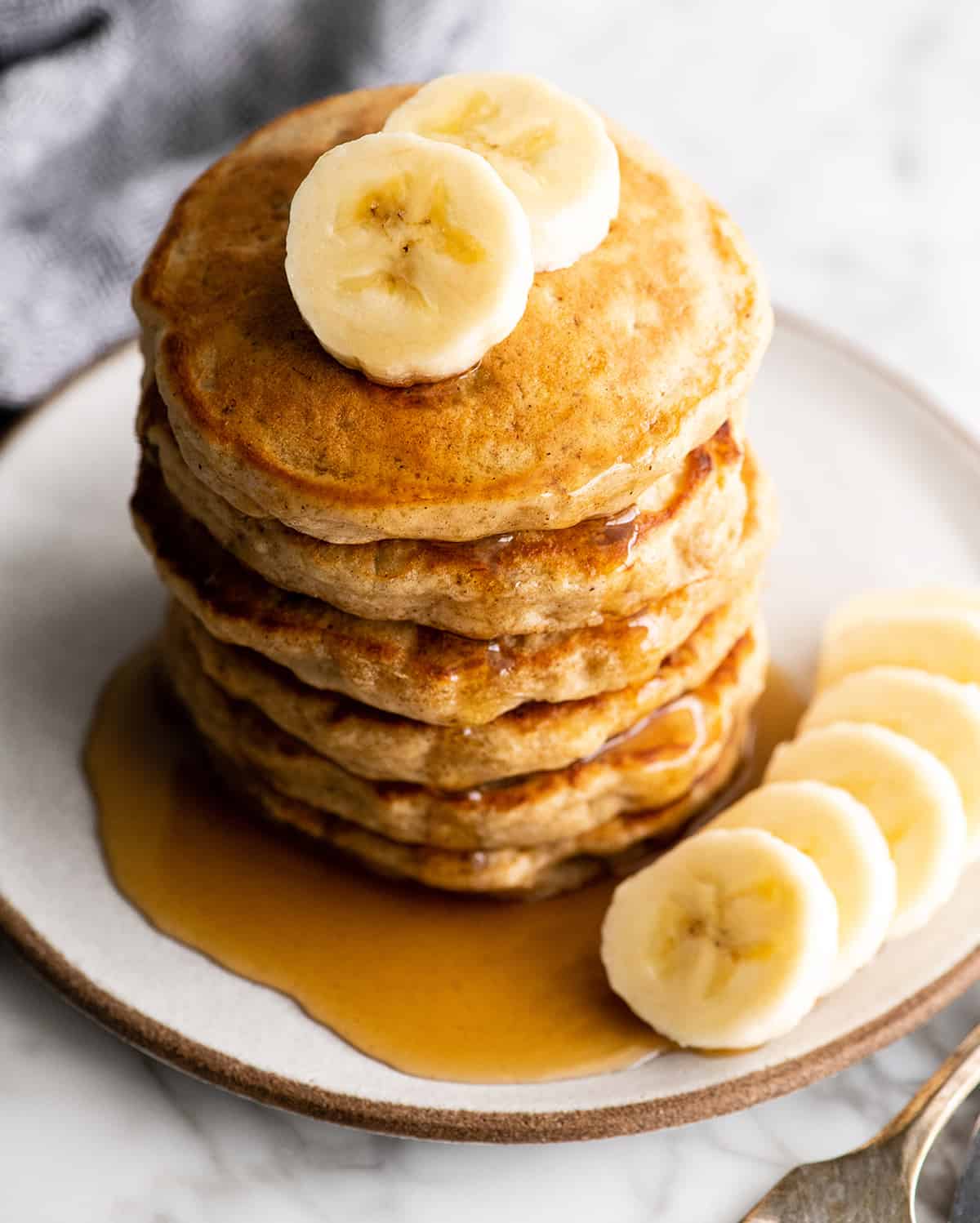 overhead view of a stack of 6 banana pancakes with syrup and bananas