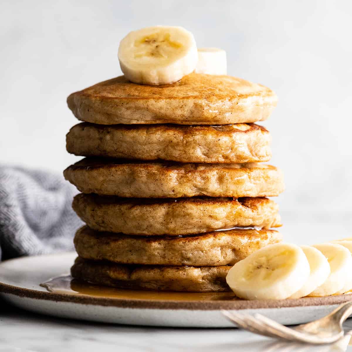 front view of a stack of 6 banana pancakes with syrup and sliced bananas
