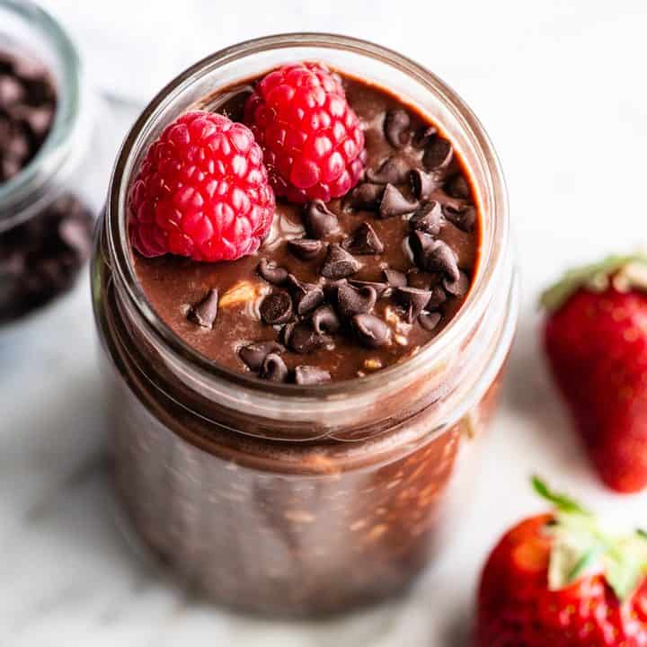 overhead view of chocolate overnight oats in a jar with raspberries and chocolate chips
