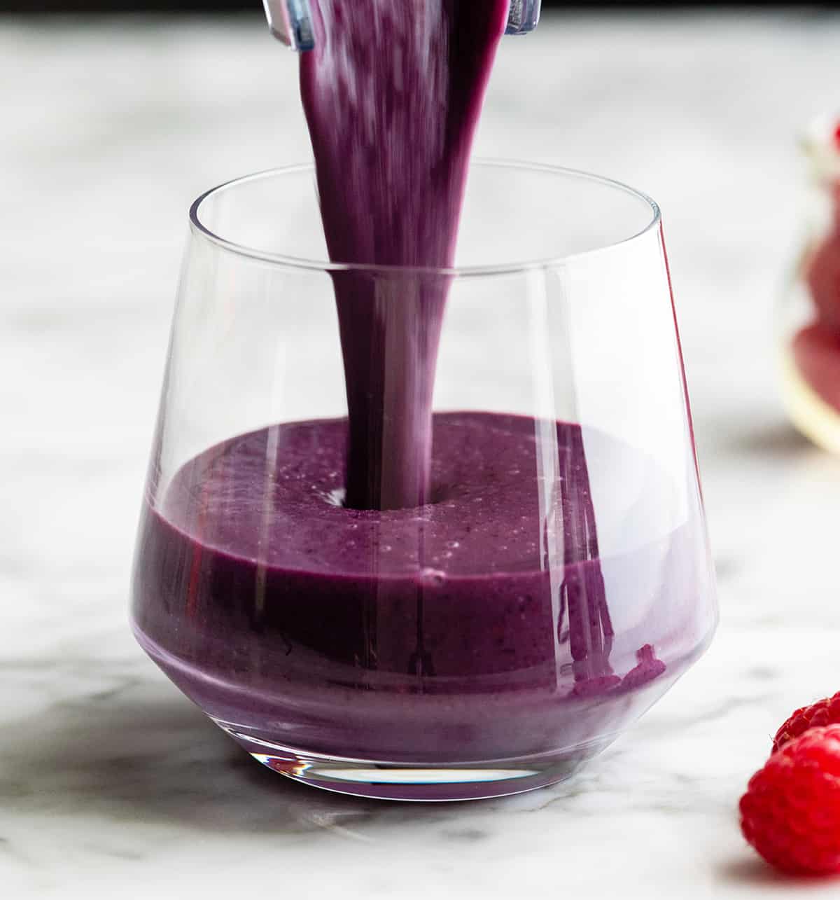 berry smoothie being poured into a glass cup
