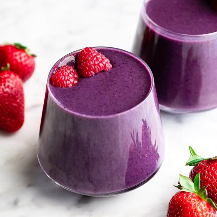 two mixed berry smoothies in glass cups topped with raspberries