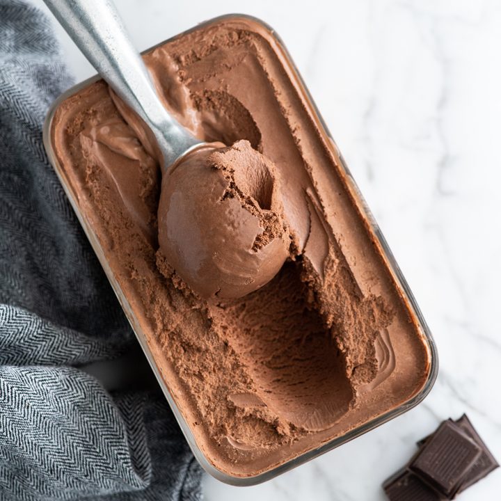 Overhead photo of an ice cream scoop scooping some chocolate ice cream out of a glass storage container