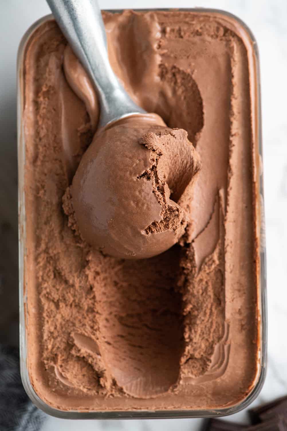 Overhead photo of an ice cream scoop scooping some chocolate ice cream out of a glass storage container