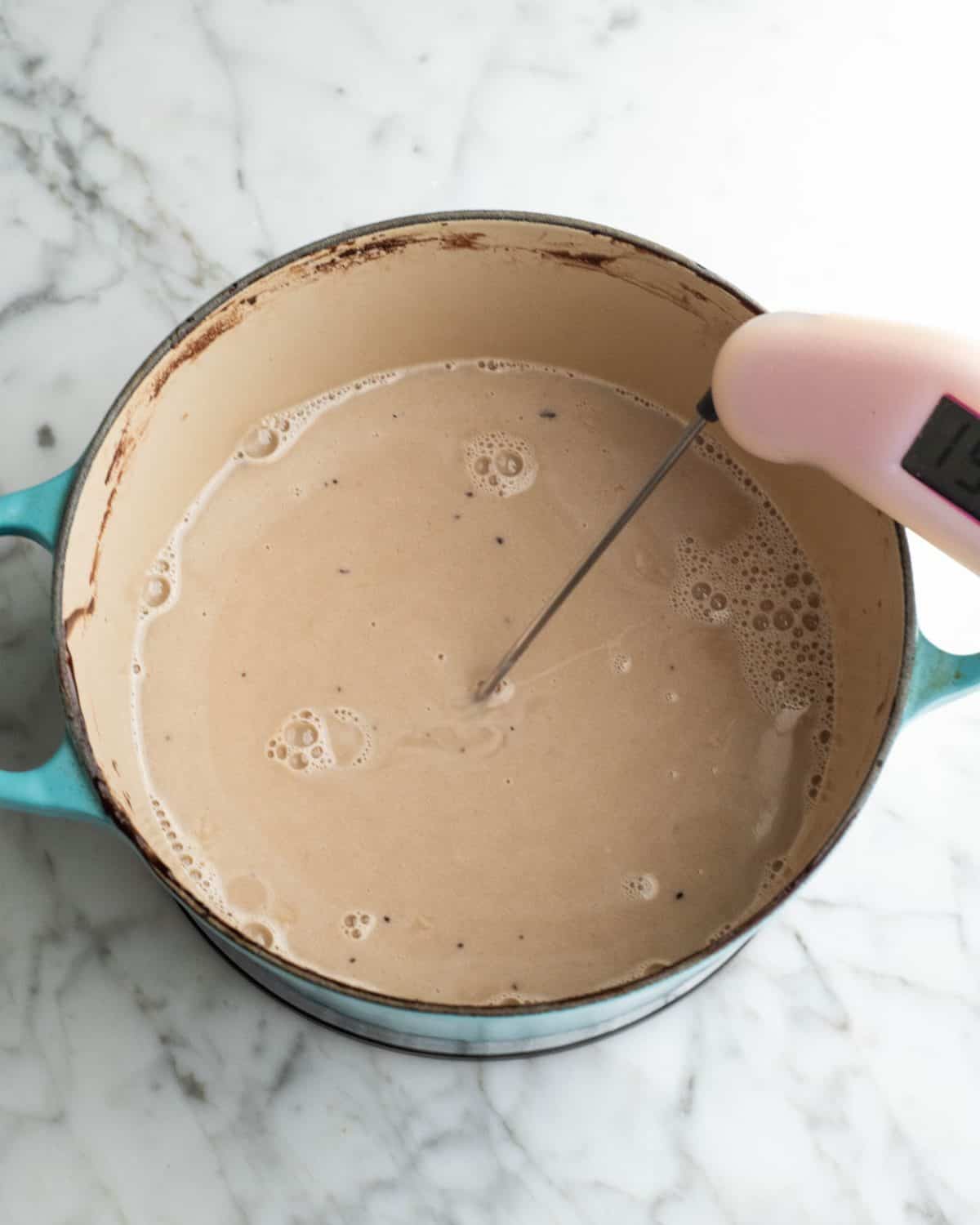 how to make chocolate ice cream - custard cooking in a blue pot, there is an instant read thermometer in the custard to check the temperature.