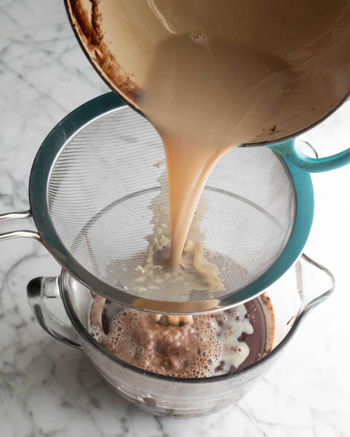 how to make chocolate ice cream - custard being poured through a fine metal strainer into a batter bowl with the rest of the chocolate ice cream base in it.