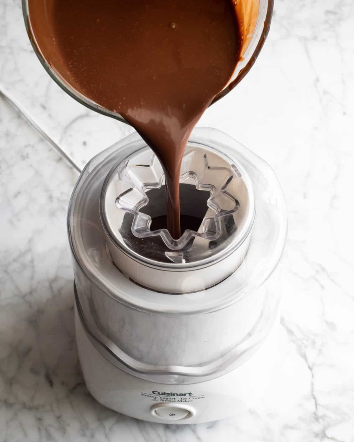 how to make chocolate ice cream - chocolate ice cream base being poured into a white ice cream maker on a marble surface.
