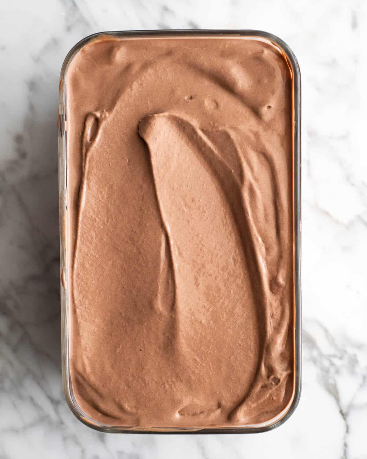 Rich, ultra-creamy, and chocolatey, this is the best homemade chocolate ice cream recipe ever! It's easy to make with only 7 ingredients (including two forms of chocolate), has a rich chocolate flavor, and is just as good as any ice cream shop! chocolate ice cream in a rectangular glass container on a marble surface to be frozen.