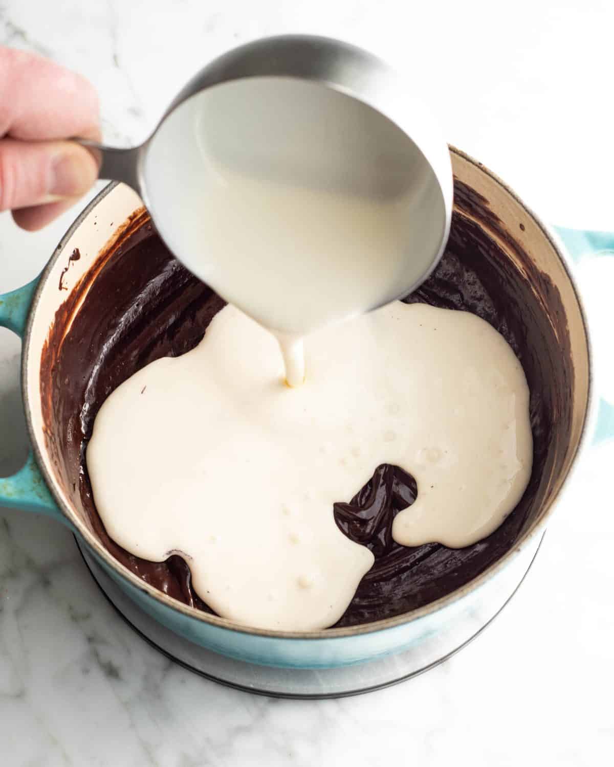 how to make chocolate ice cream - cream being poured from a metal measuring cup into the chocolate mixture in a blue pot