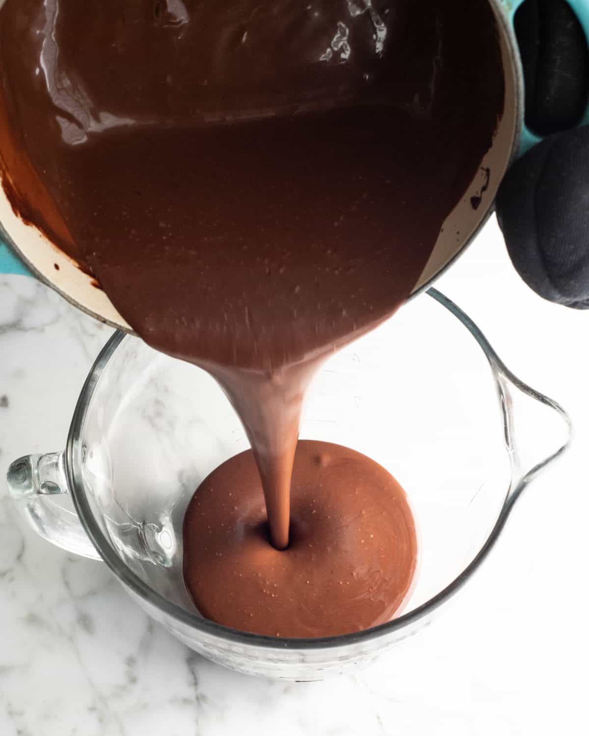 how to make chocolate ice cream - chocolate base being poured into a glass batter bowl on a marble surface from a blue pot