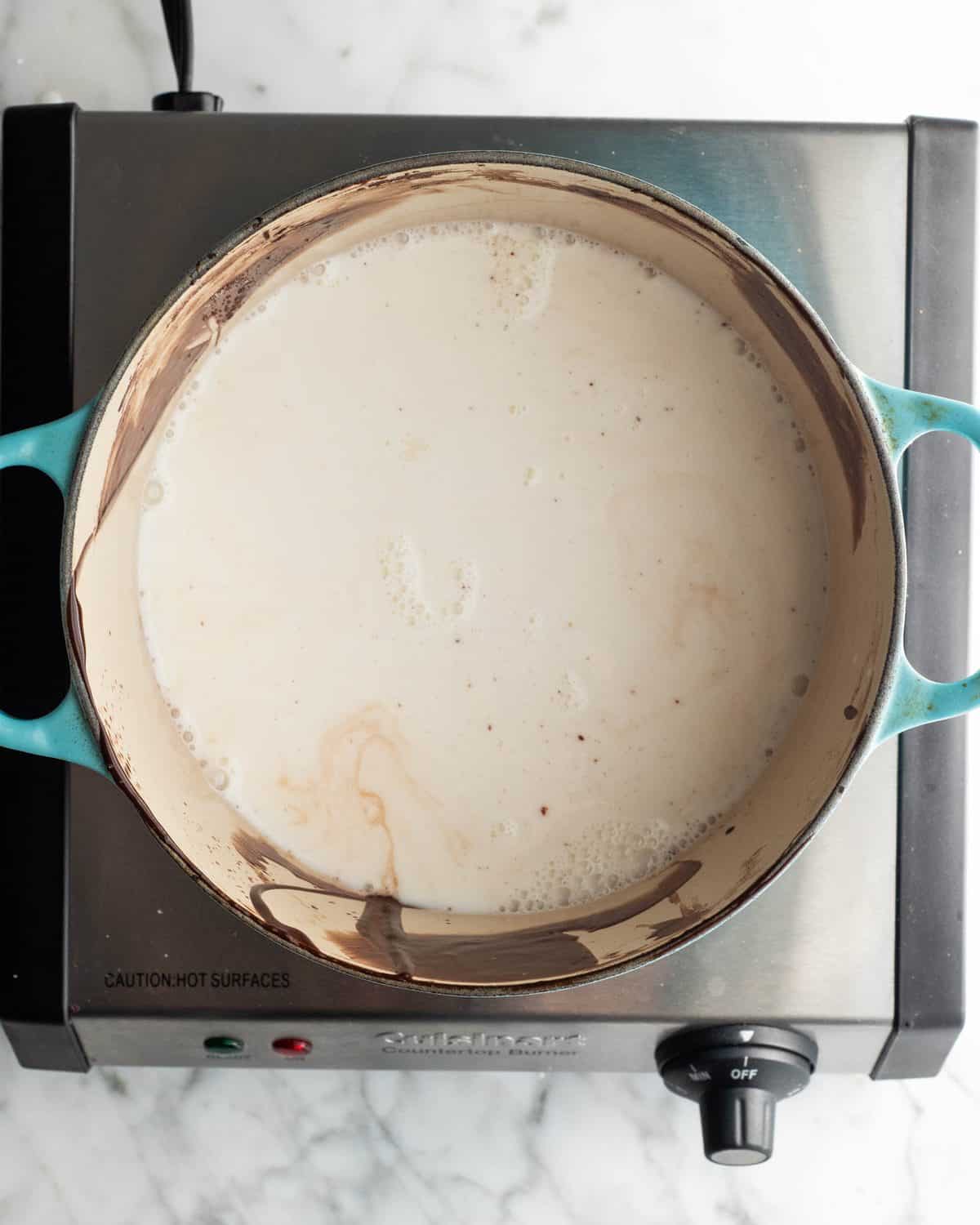 how to make chocolate ice cream - milk, sugar and sea salt being warmed in a blue pot on a metal hot plate