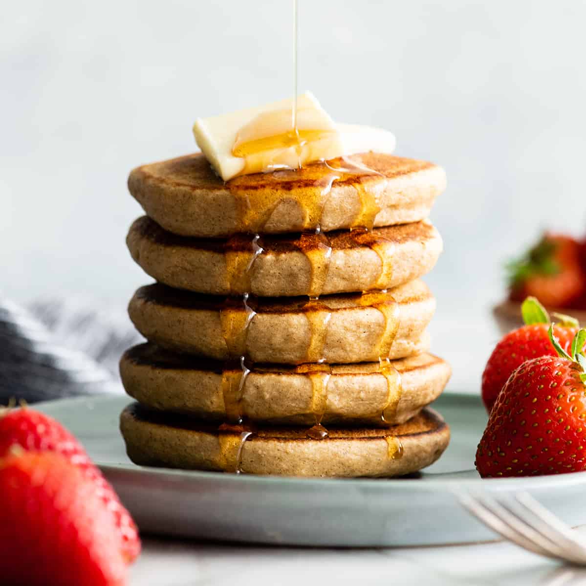 front view of a stack of 5 banana oatmeal pancakes with syrup pouring on the top