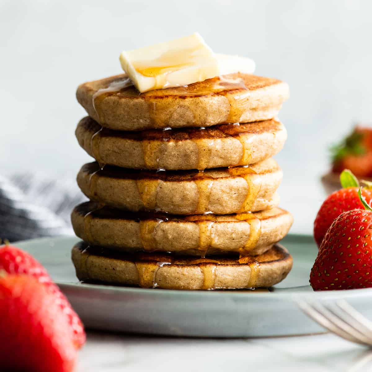 Front view of a stack of 5 banana oatmeal pancakes with butter and syrup
