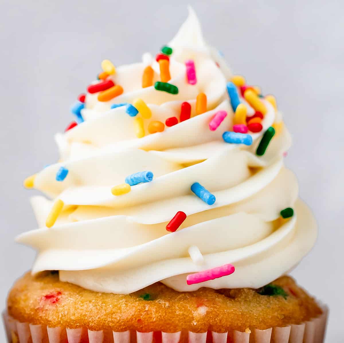 vanilla frosting piped on top of a cupcake with sprinkles