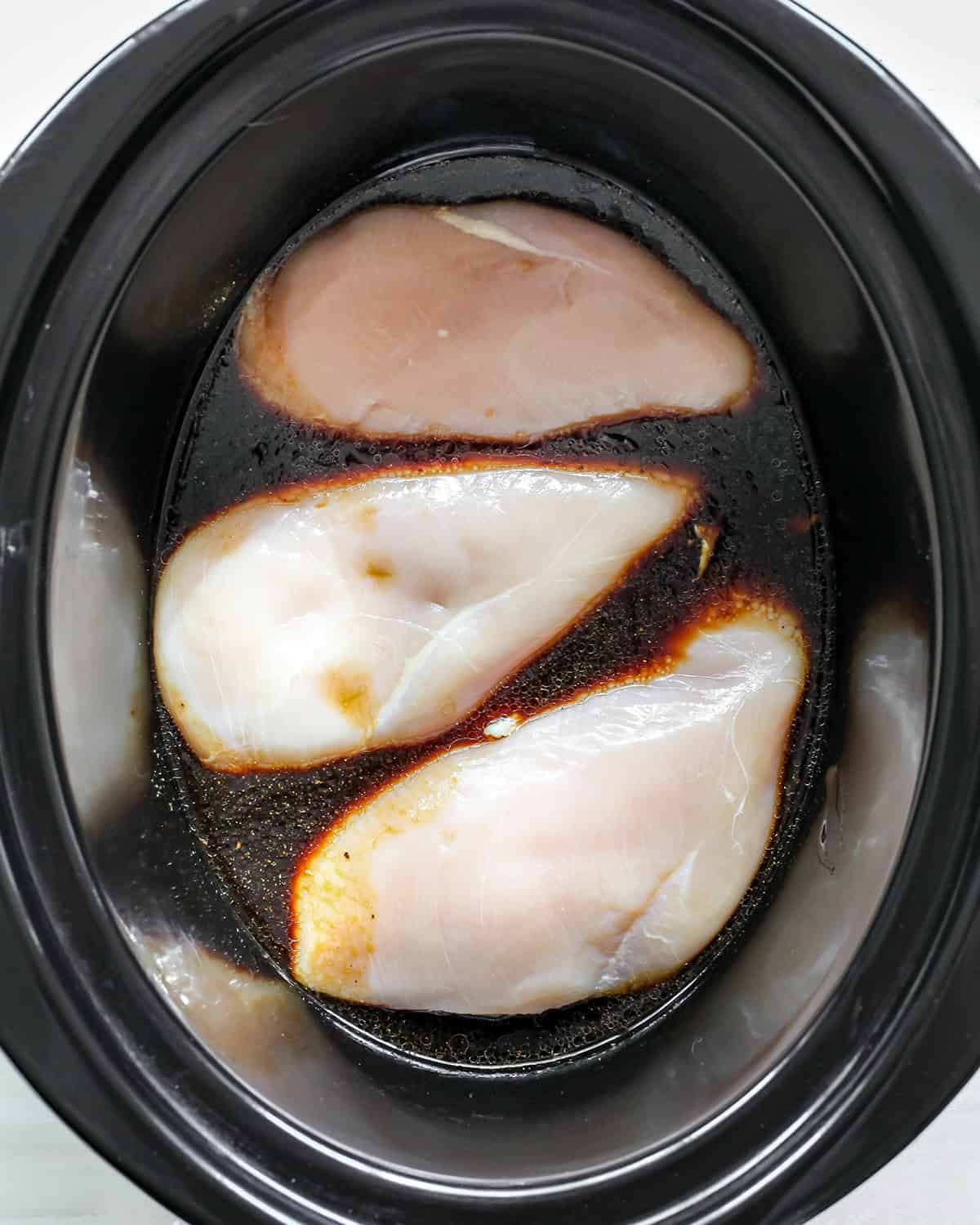 making slow cooker teriyaki chicken - three chicken breasts in the sauce in a crock pot before cooking