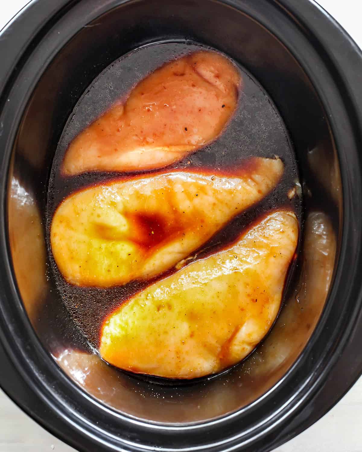 making slow cooker teriyaki chicken - three chicken breasts in the sauce in a crock pot coated with sauce before cooking