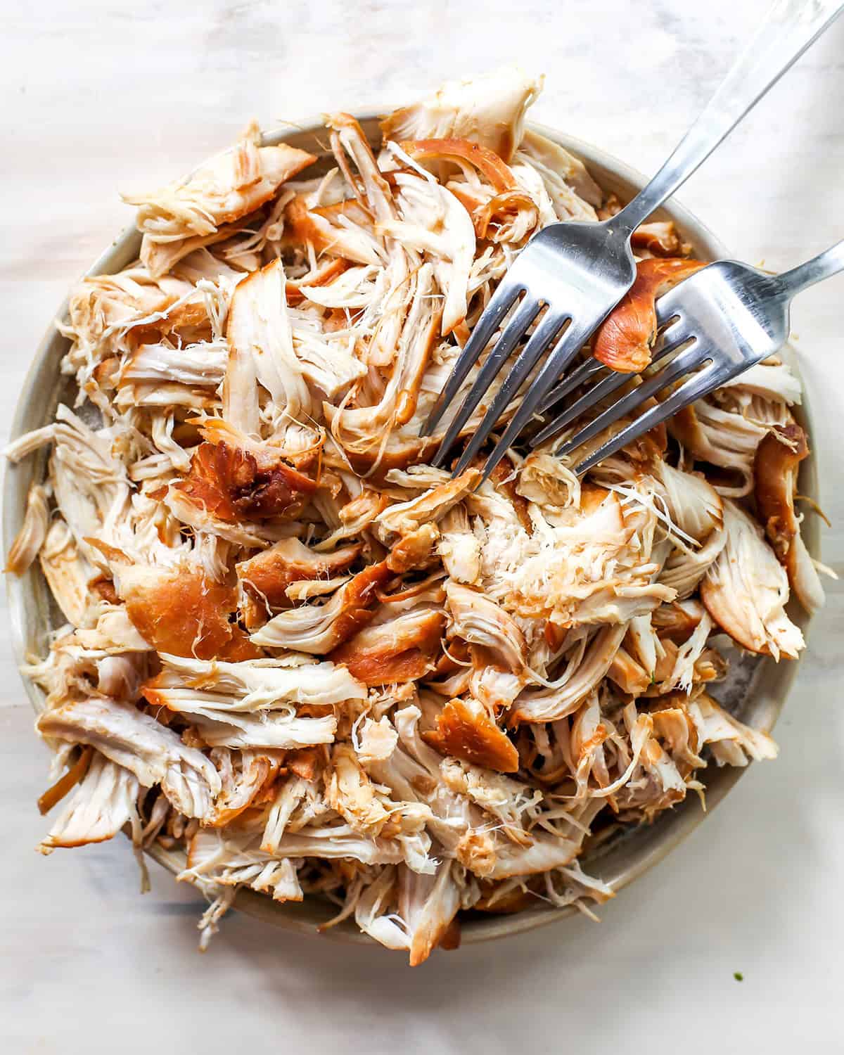 slow cooker teriyaki chicken - being shredded in a bowl with two silver forks. 