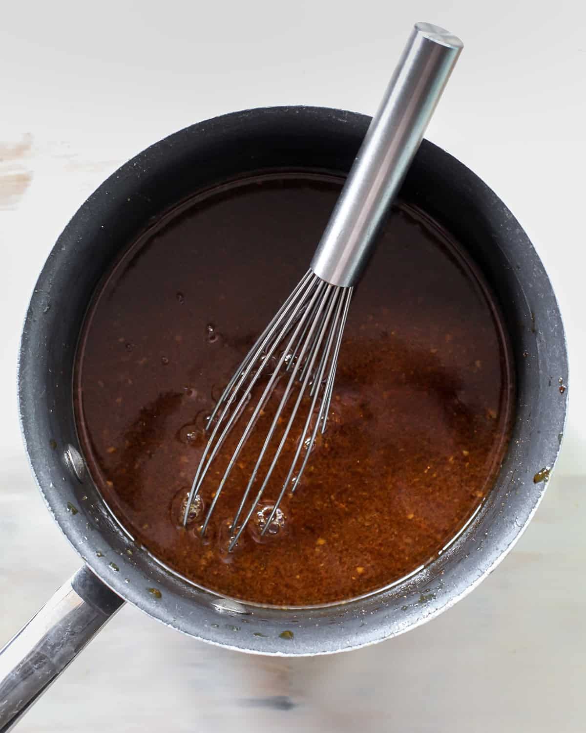 finished crock pot teriyaki chicken sauce in a saucepan with a metal whisk.