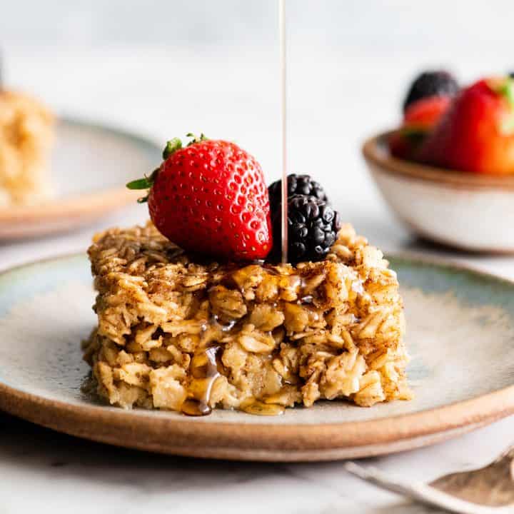 front view of syrup pouring onto a piece of baked oatmeal with berries