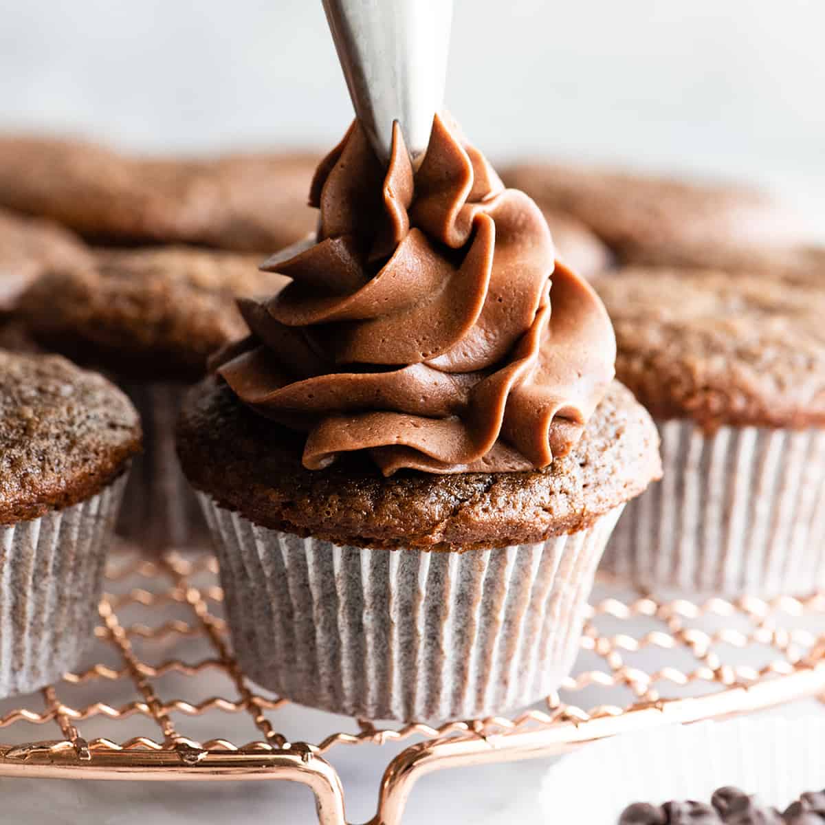 a photo of Chocolate Buttercream Frosting being piped onto a chocolate cupcake