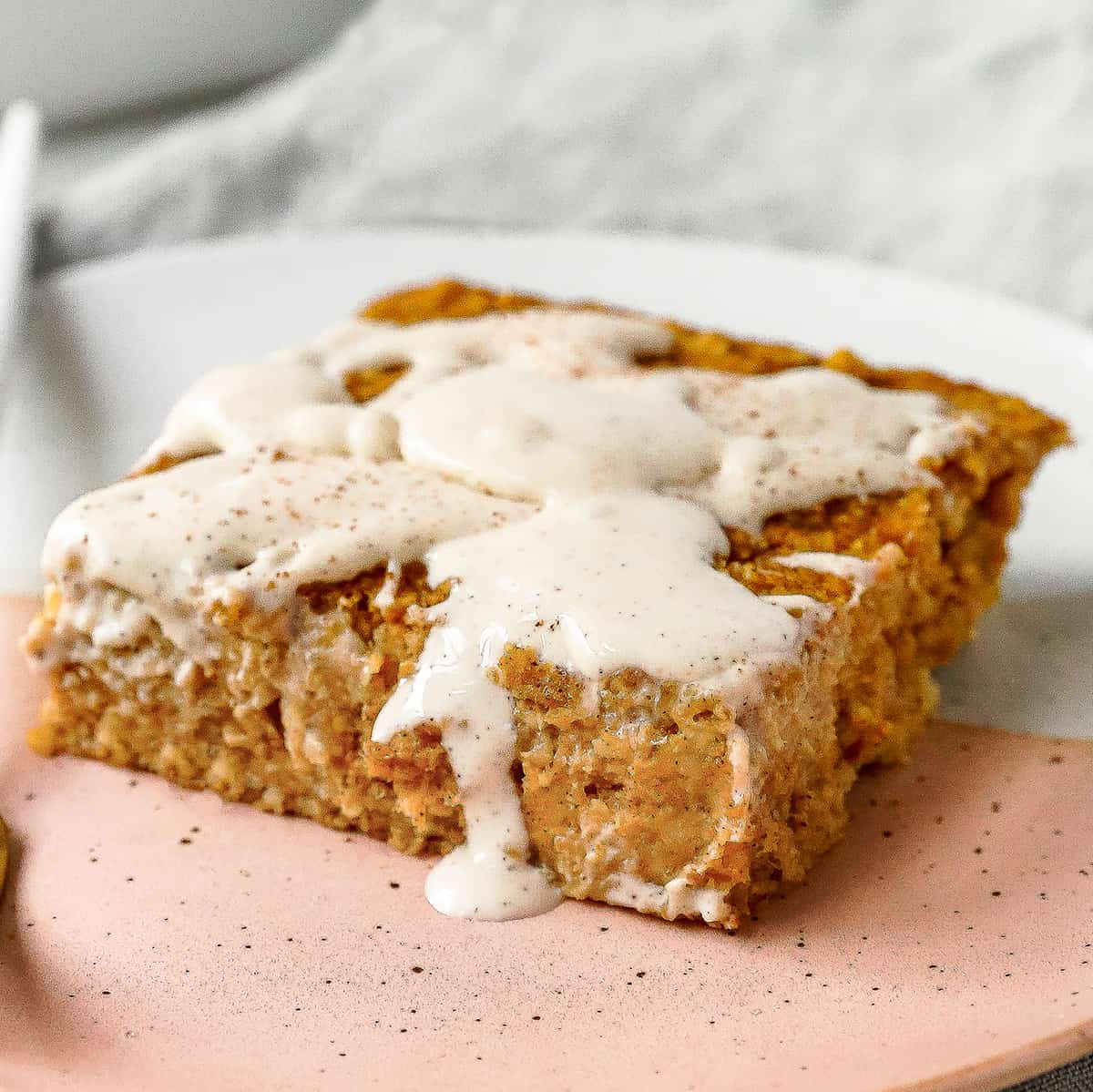 a piece of pumpkin baked oatmeal on a plate with cream cheese glaze and cinnamon